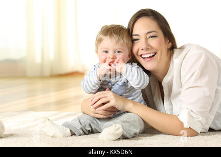 Smiley madre e il suo bambino guardando è sdraiato sul pavimento a casa Foto Stock