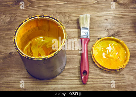 Vernice gialla può con un pennello su un rustico sfondo di legno Foto Stock