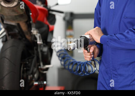 Close up di un motociclo meccanico a mano che tiene una pistola pneumatica in una officina meccanica Foto Stock