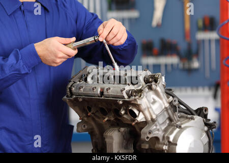 In prossimità di una motocicletta mani meccaniche utilizzando uno strumento per la riparazione di un motore in una officina meccanica Foto Stock