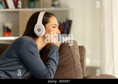 Donna rilassarsi ascoltando musica e guardando lontano attraverso una finestra seduto su un divano nel salotto di casa Foto Stock