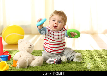 Vista anteriore verticale di un happy baby giocare con giocattoli su un tappeto a casa Foto Stock