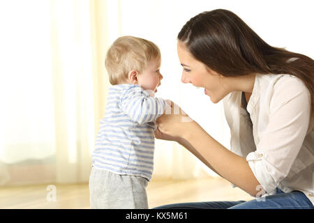 Mamma orgogliosa aiutando il suo bambino figlio nei suoi primi passi a casa Foto Stock