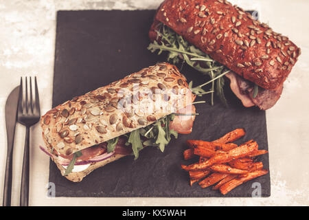 Panini con la ciabatta, carne, pancetta, verdure e salsa di panna e la patata dolce patate fritte sul nero ardesia. Foto Stock