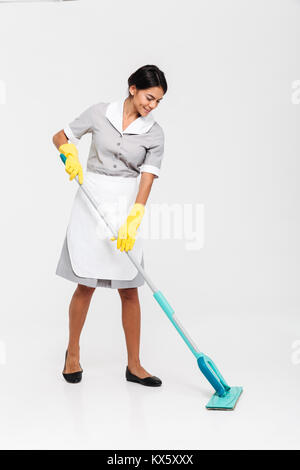 A piena lunghezza Ritratto di giovane donna attraente in una pulitura uniforme piano con mop, isolato su sfondo bianco Foto Stock