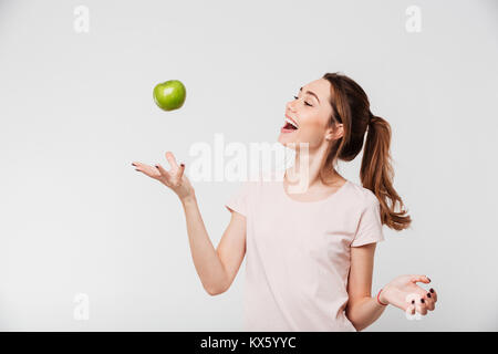 Ritratto di una sorridente ragazza felice gettando apple nell'aria isolate su sfondo bianco Foto Stock