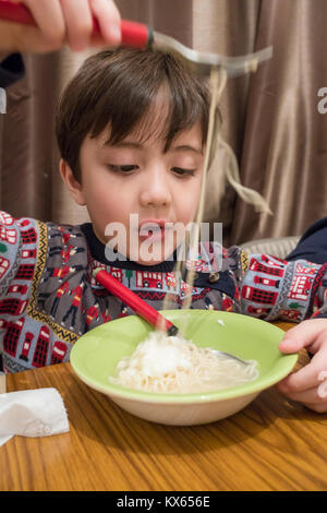 Un ragazzo si siede al tavolo da pranzo e mangia una ciotola di instant soupy tagliatelle. Foto Stock