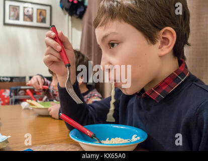 Un ragazzo si siede al tavolo da pranzo e mangia una ciotola di instant soupy tagliatelle. Foto Stock