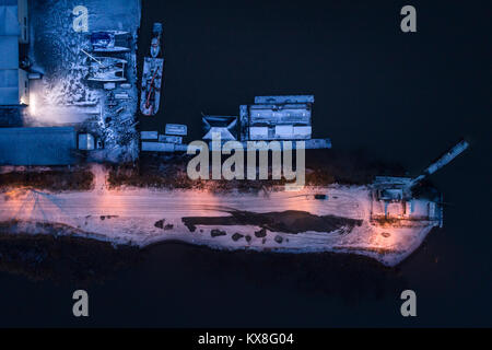 Vista aerea della barca cantiere di riparazione e strada innevata da un mare illuminato da luci di strada Foto Stock