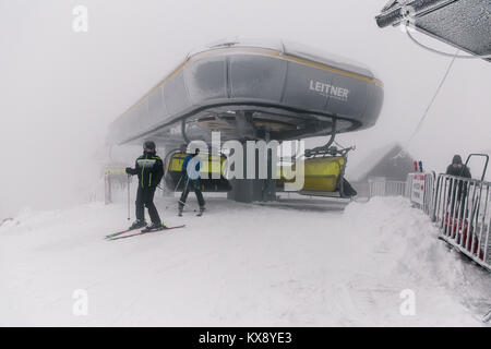 Gli sciatori getting della seggiovia sul vertice del Skrzyczne mountain ricoperta di neve in una nebbiosa giornata invernale in Szczyrk ski resort in Polonia Foto Stock