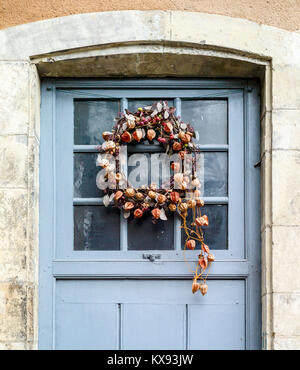 Vista frontale di una corona di Natale fatta di fiori secchi e piante in toni pastello appesa su una porta olandese vetrata. Foto Stock
