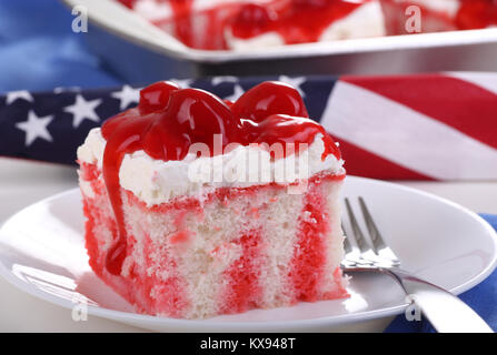 Pezzo di rosso e bianco con torta di ciliegie sulla parte superiore con la bandiera americana in background Foto Stock