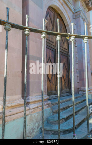 Close-up di un'anziana recinzione in ferro, un vecchio edificio in pietra con gradini in pietra e splendidamente scolpito, arcuata di doppie porte in legno con una pietra ad arco telaio Foto Stock