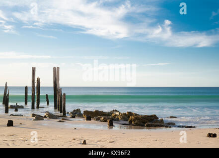 Porto Willunga Beach con il molo iconico rovine nella luce del giorno con una lenta velocità di otturatore accentuando la lunga ondata di rotolamento in arrivo. Trova i Foto Stock