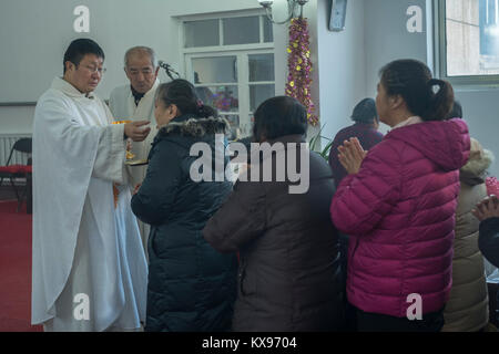 Il Reverendo Pang Ruowang di dare la comunione ai fedeli durante la Messa di Natale al Sacro Cuore di Gesù chiesa nel villaggio di Housangyu, 70 chilometri a ovest di Pechino, una delle più antiche chiese in Cina. 25-Dec-2017 Foto Stock