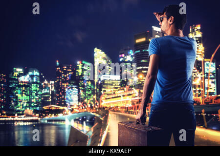 Uomo con valigia sul ponte del Giubileo a Singapore di notte Foto Stock