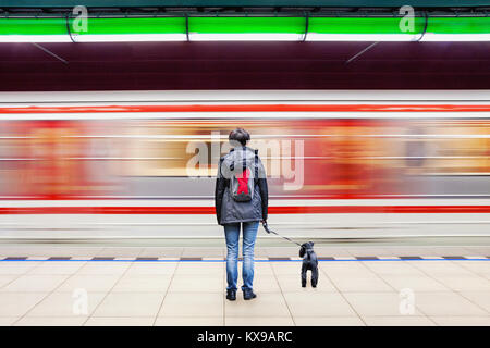 Lonely donna con cane presso la stazione della metropolitana della piattaforma con sfocata movimento del treno in background Foto Stock
