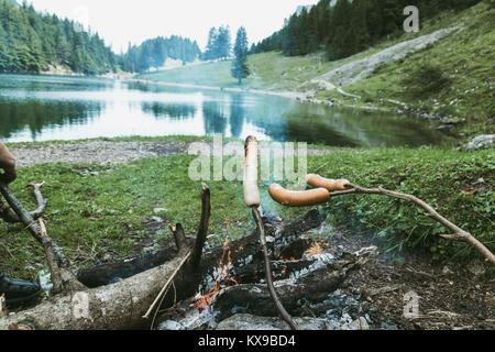 I bastoncini di legno per barbecue grill salsicce sul caminetto di fronte lago di montagna Foto Stock