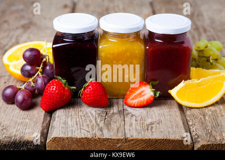 Tre vasi con marmellata su un sfondo di legno. Deliziosi dessert e frutta fresca di close-up. Foto Stock