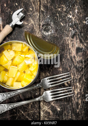 Conserve di ananassi in un barattolo di latta con forche e apriporta. Su uno sfondo di legno. Foto Stock