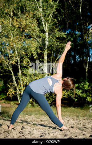La donna a praticare yoga nella sabbia - triangolo pongono - Utthita Trikonasana - giorni di autunno Foto Stock