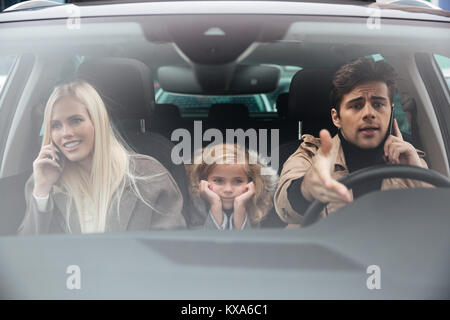 Immagine del triste ragazza seduta in auto mentre la madre e il padre parlando da telefoni cellulari. Guardando a parte. Foto Stock