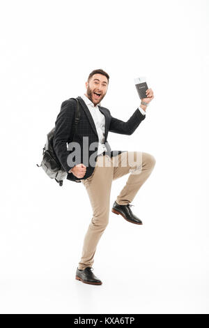 A piena lunghezza Ritratto di un gioioso eccitato uomo con passaporto con i biglietti di volo e celebrando isolate su sfondo bianco Foto Stock