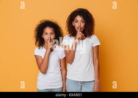 Ritratto di due graziose afro american sorelle e permanente che mostra il silenzio gesto isolato su sfondo arancione Foto Stock