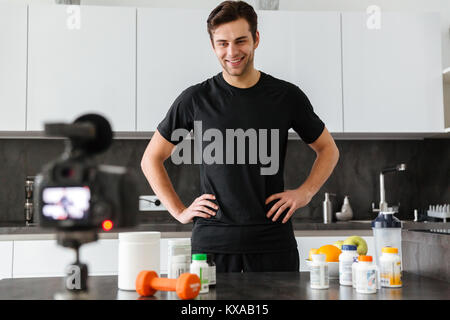 Felice giovane riprese il suo video blog puntata sul cibo sano additivi stando in piedi sul tavolo della cucina Foto Stock