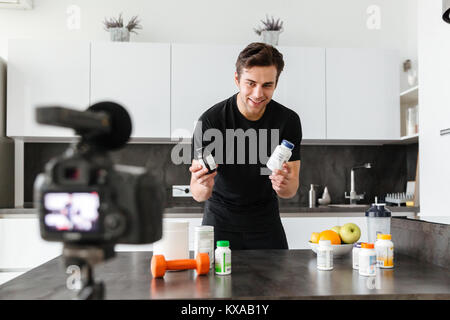 Eccitato giovane riprese il suo video blog puntata sul cibo sano additivi stando in piedi sul tavolo della cucina Foto Stock