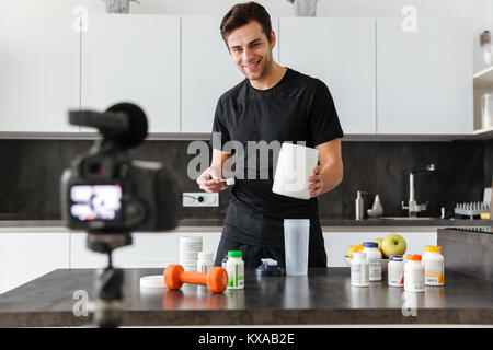 Felice giovane riprese il suo video blog puntata sul cibo sano additivi stando in piedi sul tavolo della cucina Foto Stock