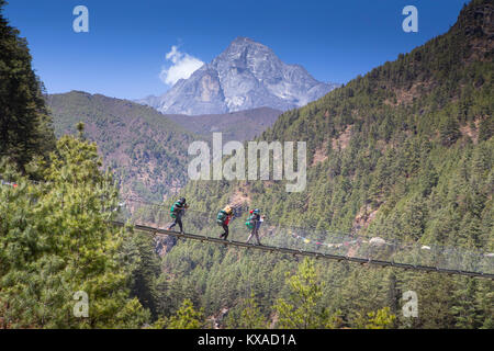 Tre portieri stanno attraversando una sospensione Nepalese ponte sopra una gola profonda sul modo di Namche Bazar. Foto Stock