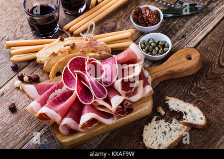 Carne affumicata antipasto platter servita con pane tostato, bastoncini di pane e di vino rosso sul tavolo di legno. Il cibo italiano, prosciutto, salame, pomodori secchi Foto Stock