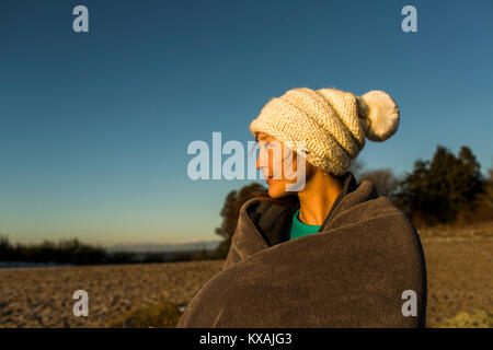Giovane donna seduta in knit hat e avvolto in una coperta durante il riposo dopo l'esecuzione in Discovery Park, Seattle, Washington sate, STATI UNITI D'AMERICA Foto Stock