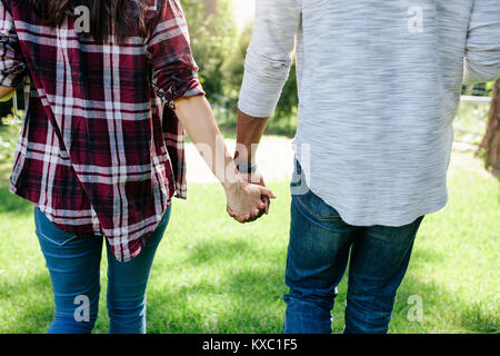 Vista posteriore di amare giovane tenendo le mani all'esterno, su data nel parco. Girato dal retro di un uomo e di una donna che cammina insieme all'esterno. Foto Stock