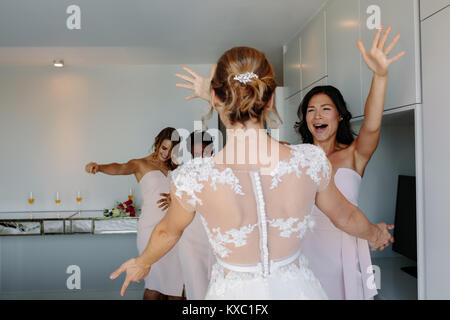Sposa e le sue damigelle hanno divertimento in camera in hotel il giorno del matrimonio. Bridesmaids abbracciando sposa il giorno del matrimonio. Foto Stock