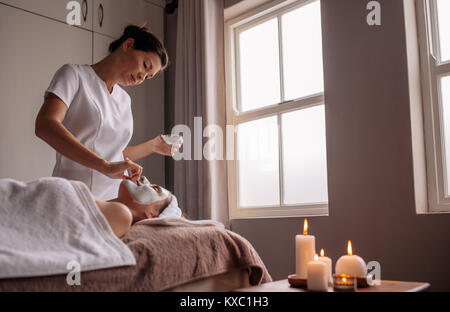 La donna la ricezione di una maschera per il viso trattamenti in un centro di bellezza e benessere dal terapista. Sperimentato cosmetico applicando la maschera per il viso sul volto femminile. Foto Stock