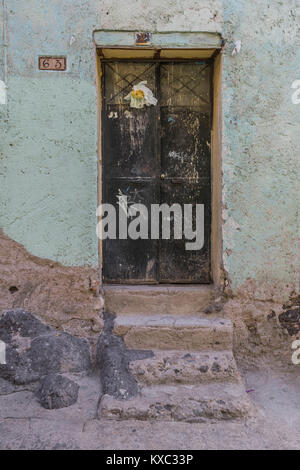 Double nero le porte di metallo con un libro bianco fiore postato sul lato sinistro, scalini in pietra e il marciapiede, e di una luce di colore verde, parete in Guanajuato, Messico Foto Stock