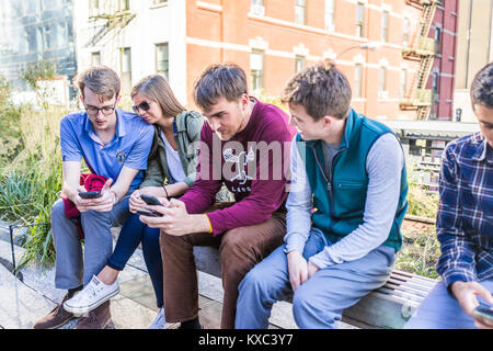 La città di New York, Stati Uniti d'America - 27 Ottobre 2017: primo piano della giovane coppia con gli amici guardando gli smartphone, telefono seduta sul banco di prova nella moderna Urban garden park Foto Stock