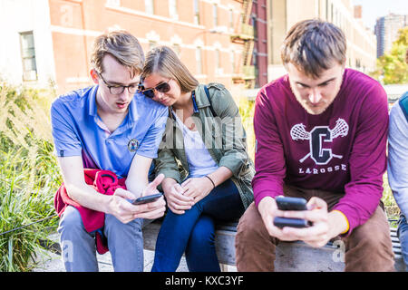 La città di New York, Stati Uniti d'America - 27 Ottobre 2017: primo piano della giovane coppia con gli amici guardando gli smartphone, telefono seduta sul banco di prova nella moderna Urban garden park Foto Stock