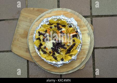 Mexican Nachos o latino-americano - Close up di fagioli neri peperoncino jalapeno sul mais tortilla chips con formaggio fuso sul piatto di legno. Foto Stock