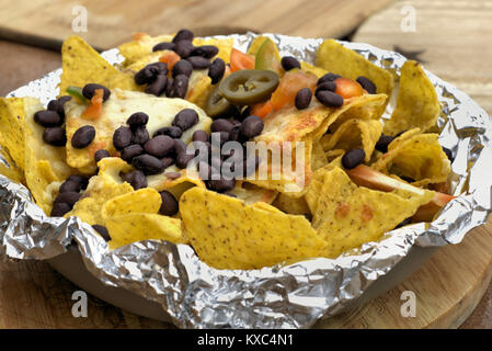 Mexican Nachos o latino-americano - Close up di fagioli neri peperoncino jalapeno sul mais tortilla chips con formaggio fuso sul piatto di legno. Foto Stock
