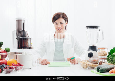 Sorridente nutrizionista professionista in possesso di un apple, ella ha sani frutti, verdure e centrifughe sulla sua scrivania; dieta sana e il concetto di benessere Foto Stock