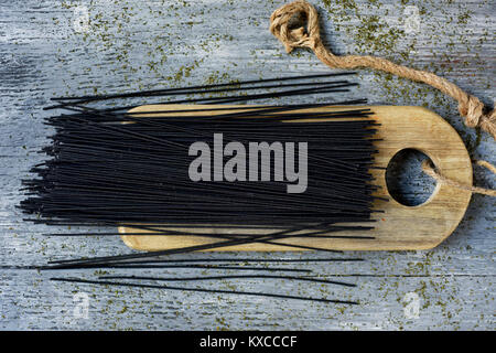Elevato angolo di visione di un mazzetto di crudo spaghetti al nero su un tagliere di legno, collocata sul grigio di una tavola in legno rustico Foto Stock