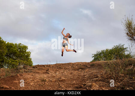 Basso angolo di visione della donna che si tuffa oltre la collina mentre esercita contro il cielo nuvoloso Foto Stock