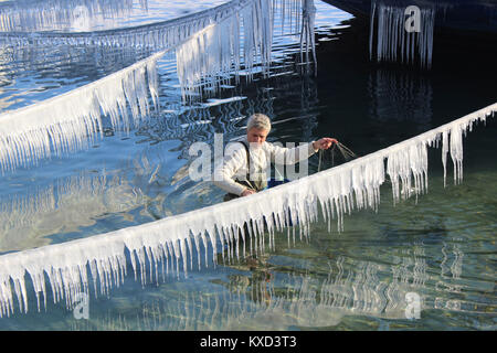 Angolo di Alta Vista del pescatore azienda rete da pesca mentre in piedi nel lago in mezzo congelati corda con ghiaccioli Foto Stock