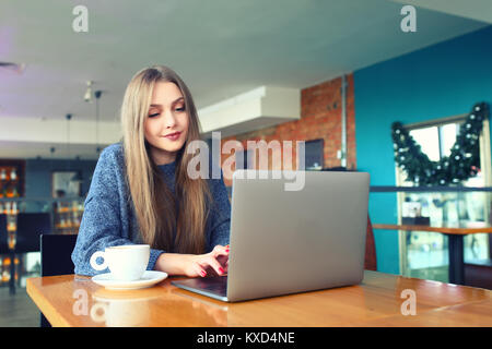 Donna al lavoro su computer portatile in una caffetteria. Giovane donna seduta al tavolo di un caffè usinglaptop. Con la copia in bianco ghiaione dello spazio per la vostra pubblicità messaggio di testo o il contenuto promozionale tonica immagine. Messa a fuoco selettiva. Foto Stock