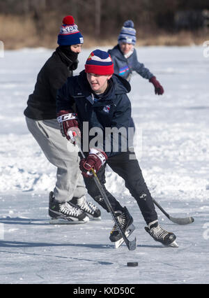 Ragazzi che giocano a hockey su ghiaccio su uno stagno ghiacciato in una giornata fredda Foto Stock