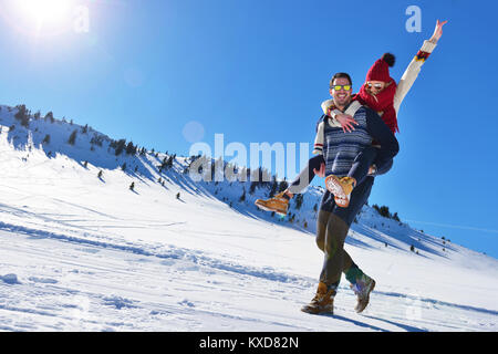 Coppia giovane divertirsi sulla neve. Felice l'uomo alla montagna dando piggyback ride per la sua ragazza sorridente. Foto Stock