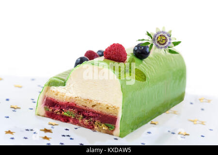 Il pistacchio Lampone Yule Log decorate con lamponi freschi, mirtillo e pasion fiore su sfondo bianco. Foto Stock